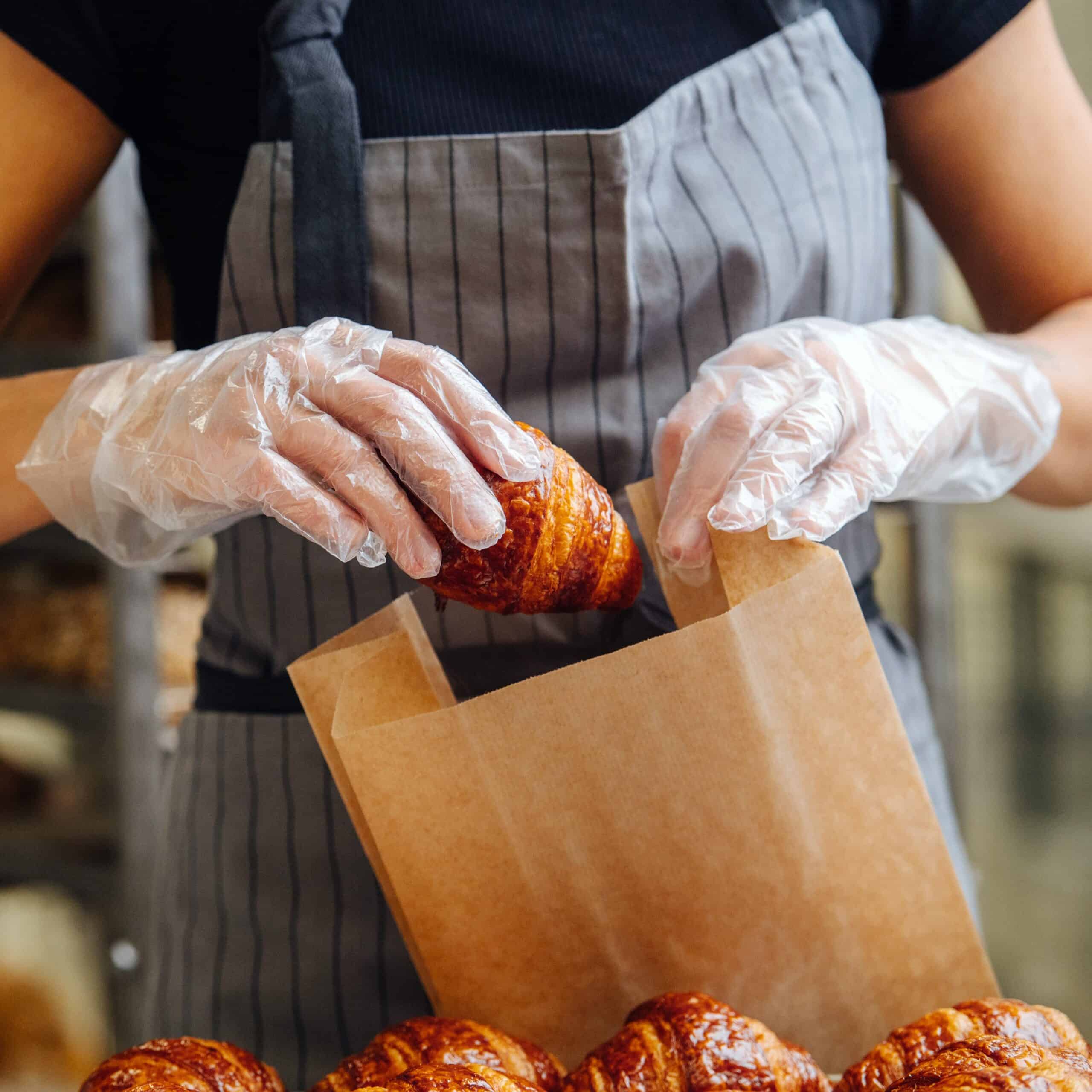 Baker,Placing,Freshly,Baked,Crispy,Golden,Croissants,In,A,Paper