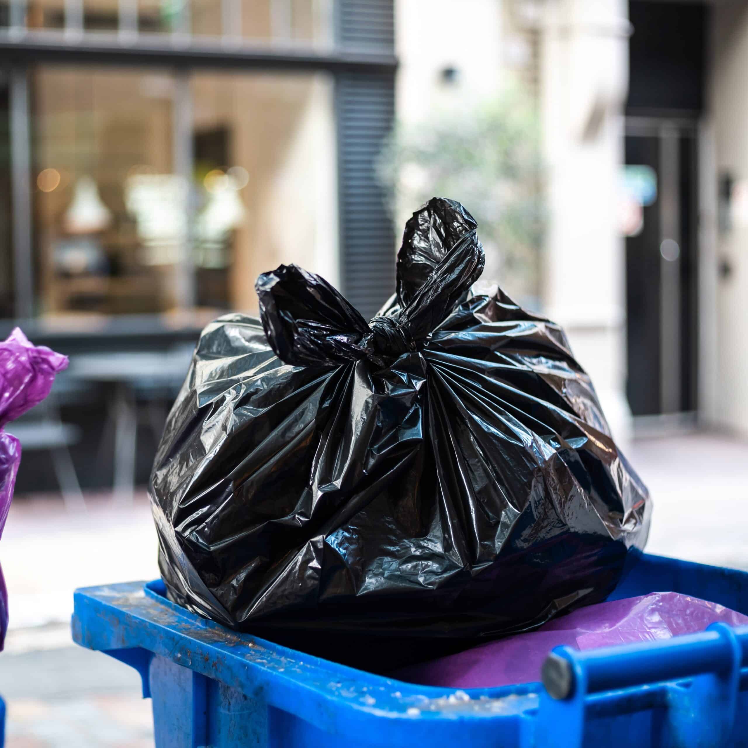 Purple and black bags of trash on a garbage bin during daytime